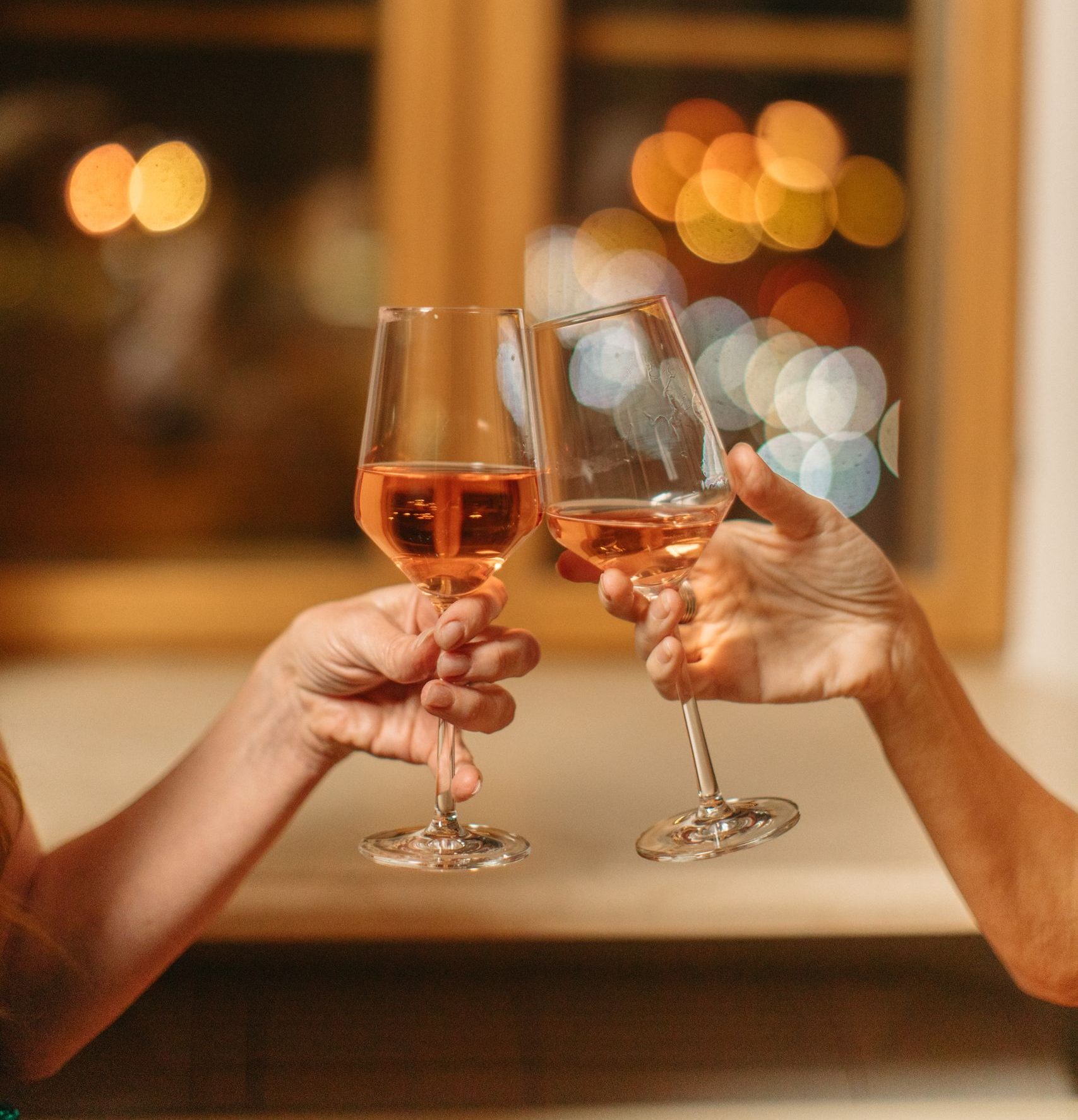 Two people clinking wine glasses in a cozy indoor setting with a blurred background.